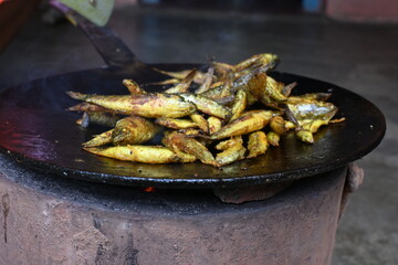 Small Snakehead or Channa orientalis Fish being fried in a pan. Fish are typically marinated with spices like turmeric, salt, and chili powder before being deep fried until they are crispy and golden.