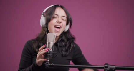 Young woman joyfully singing into a microphone with headphones in a studio - Powered by Adobe