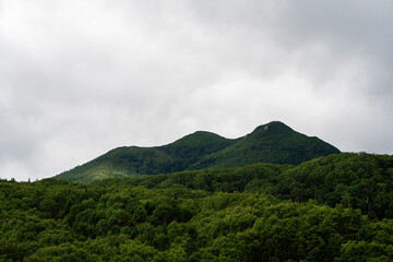 Dense green forest covers the rolling mountain slopes while heavy clouds gather above, creating a dramatic and moody atmosphere in this scenic summer landscape. Nature of Sakhalin Island