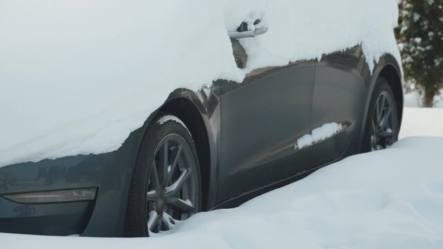 Snow covered electric car parked on street. Challenges and nuances of operating car and charging battery in winter. Preparing to drive after heavy snowfall.