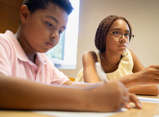 Afro students focusing on schoolwork at a desk, learning and writing during class