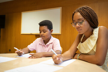 Afro students writing exams or schoolwork while sitting at a table in a classroom
