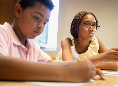 Afro students focusing on schoolwork at a desk, learning and writing during class - Powered by Adobe