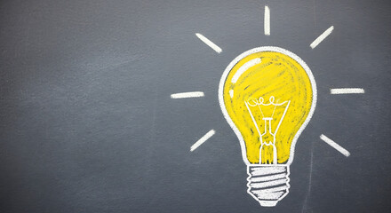 Hand-drawn bright yellow lightbulb on a dark chalkboard surface. Concept of creative thinking, inspiration, and bright ideas