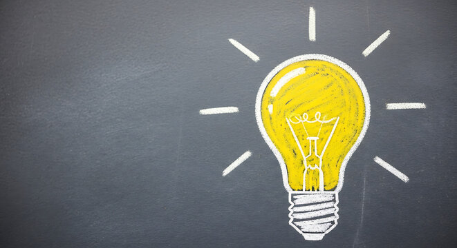Hand-drawn bright yellow lightbulb on a dark chalkboard surface. Concept of creative thinking, inspiration, and bright ideas