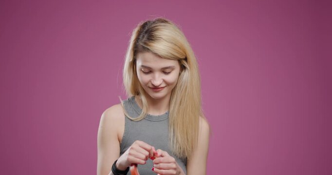 Young blond woman examining orange duct tape against a pink background