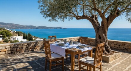 Fototapeta premium Outdoor dining scene; table set with plates and cups under a large olive tree. Ocean and distant hills in the background on a sunny day