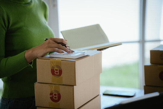 A young female entrepreneur managing online orders, packing parcels, and running a small e-commerce business with professionalism and happiness.
