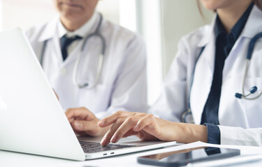Obraz premium Two asian doctors discuss diagnosis, analyzing data on laptop in hospital office. Male and female medical professionals have a patient case conference, using laptop at doctor's office, close up
