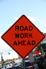 warning sign in diamond shape orange color displaying ROAD WORK AHEAD