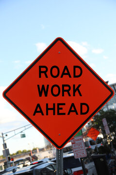 warning sign in diamond shape orange color displaying ROAD WORK AHEAD