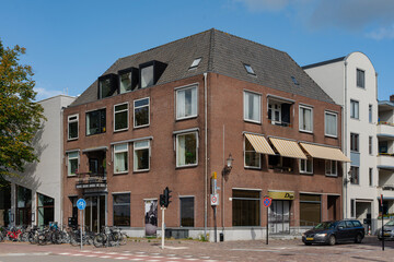 Brick corner building with awning, windows, and grey roof on a city street with parked bicycles.