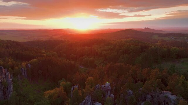 An aerial drone view captures the stunning sunset over the majestic sandstone rock formations and lush forests of Prachovsk&eacute; sk&aacute;ly in the Bohemian Paradise region of the Czech Republic. The warm, gold