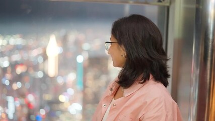 Portrait of Indian woman looking at night view of Dubai city from 124th floor of Burj Khalifa building in Dubai, UAE. Aerial cityscape view from top floor skyscraper window. Colorful bokeh background - Powered by Adobe