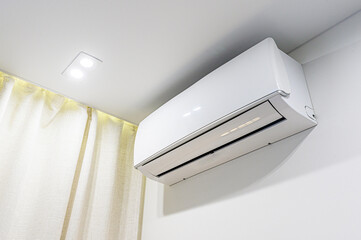 A white air conditioner unit mounted on a wall in a room with a light and curtain