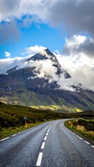 Fototapeta premium Asphalt road curves toward majestic mountain peak, shrouded in clouds