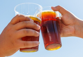 Two people are holding up two cups of beer