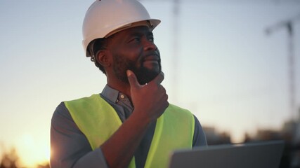 Inspired african american man looking at construction site and dreaming. Portrait of professional builder, foreman or engineer examining new building in city, medium shot with black man in helmet