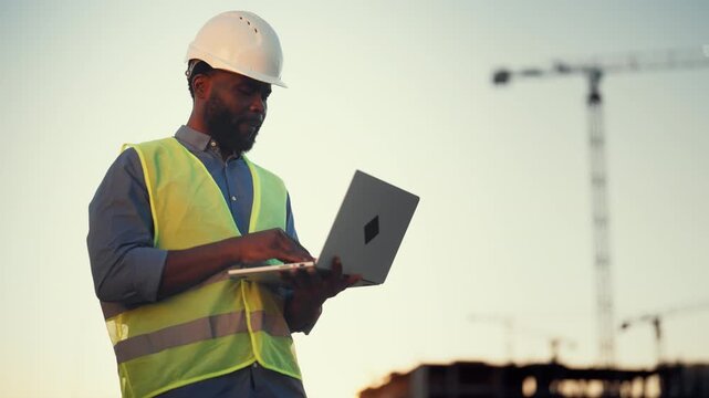 Modern technology and software for architect and builders, black man with laptop . Inspector or auditor checking quality of building, professional engineer on construction site, african ethnicity