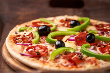 Pizza with chorizo ​​sausage, mozzarella cheese, green pepper and black olives. Rustic wooden background. Soft focus.	