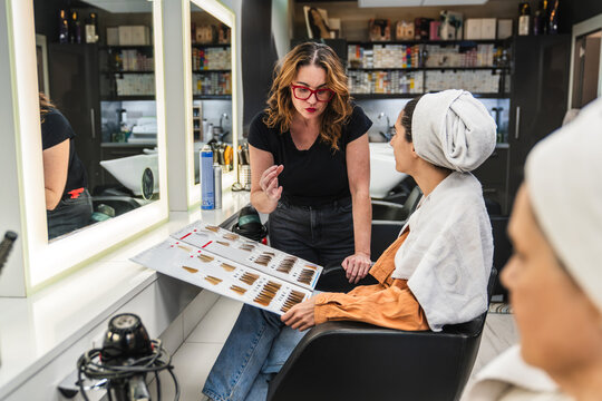 Hair stylist presenting a hair dye chart to a woman with a towel on her head, advising on color selection