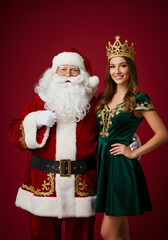 Santa Claus and woman in crown and green dress on red background  