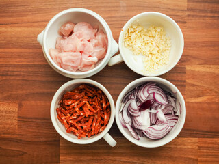 Four white porcelain small cups filled with chopped raw chicken, chorizo sausage, garlic and onions, Food preparations. Cooking dinner concept.