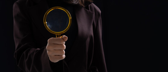 Woman holding magnifying glass in focus, representing investigation or inspection concept in a...