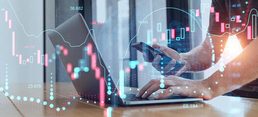 Businessman analyzing financial market data on laptop and smartphone with digital stock charts and graphs overlayed on transparent futuristic interface.