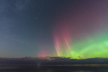 Celestial spectacle: Colorful aurora borealis with pink and green lights dances in the starry sky over the Baltic Sea, Estonia.