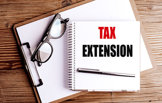 Notebook with text tax extension on wooden desk with clipboard, glasses and pen