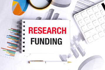 Notebook with text research funding on financial documents with calculator and pen on white desk
