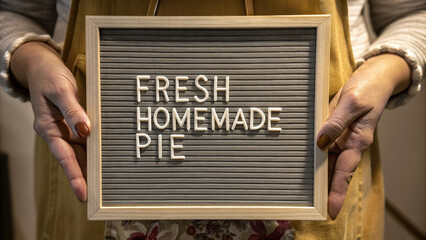 Fresh homemade pie signboard held by person with painted nails, cozy warm clothing, and floral skirt, inviting and comforting message