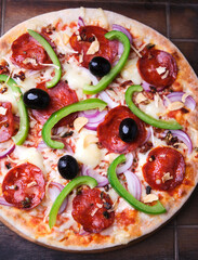 Pizza with chorizo ​​sausage, mozzarella cheese, green pepper and black olives. Rustic wooden background. Soft focus.	