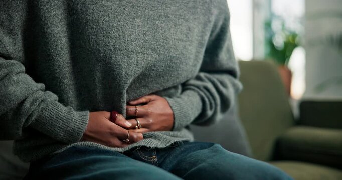 Abdomen, cramps and hands of woman on sofa in living room of home for menstruation or stomach pain. Medical, menstrual cycle and period with person rubbing belly in apartment for discomfort or nausea