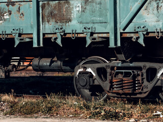 Naklejka premium Extreme close-up on the wheels and bogey of a rusty teal freight car, showing the heavy industrial mechanisms and textures of the railway transport.