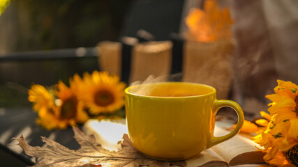 Cozy autumn scene with a steaming cup of tea and sunflowers.