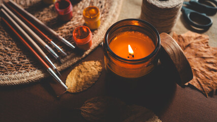 Cozy autumn still life with a lit candle, paintbrushes, and fall leaves.