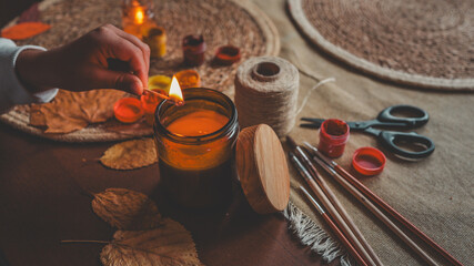 Cozy autumn scene with a lit candle and craft supplies on a wooden table.