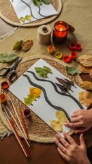 Fototapeta premium Autumn leaf art project with a lit candle and craft supplies.
