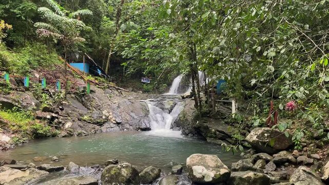 Tiered jungle waterfall pours into a turquoise pool at Salakot Falls in Puerto Princesa, Palawan, Philippines. Wide static shot with lush rainforest, rocks, and gentle flow in daylight.