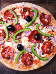 Pizza with chorizo ​​sausage, mozzarella cheese, green pepper and black olives. Rustic wooden background. Soft focus.	