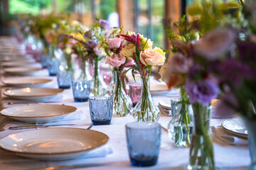 A beautifully decorated wedding or celebration event table with colorful flowers, vintage plates, and cutlery in soft natural light.The space blends modern, rustic,retro elements with charming chairs.