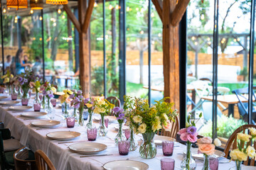 A beautifully decorated wedding or celebration event table with colorful flowers, vintage plates, and cutlery in soft natural light.The space blends modern, rustic,retro elements with charming chairs.
