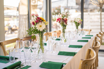 A beautifully decorated wedding or celebration event table with colorful flowers, vintage plates, and cutlery in soft natural light.The space blends modern, rustic,retro elements with charming chairs.