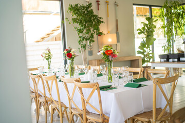 A beautifully decorated wedding or celebration event table with colorful flowers, vintage plates, and cutlery in soft natural light.The space blends modern, rustic,retro elements with charming chairs.