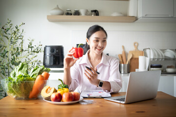 Smiling female nutritionist holding red bell pepper while giving online consultation on laptop. Concept of telehealth, and remote wellness.