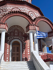 Traditional Greek Orthodox Church entrance with Greek flag and ornate architecture under blue sky