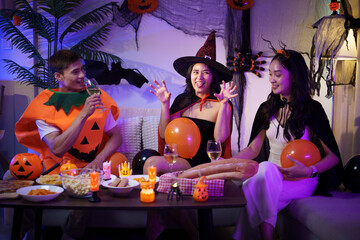 Friends celebrating Halloween together at home, wearing festive costumes and enjoying drinks in a...
