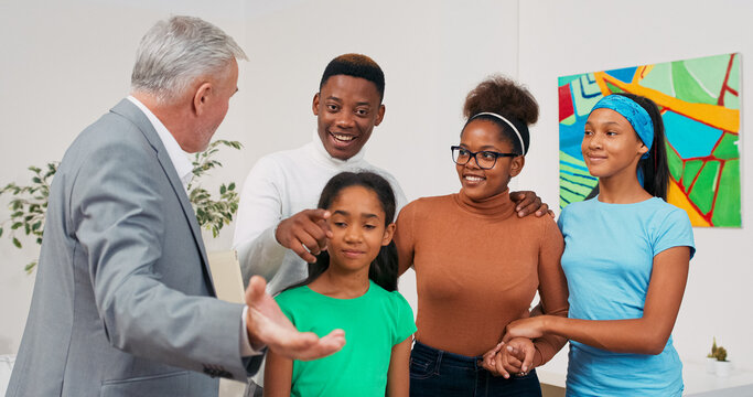 The real estate agent presents the apartment to a smiling couple and their children. He points to key features of the space while the family looks around with joy.